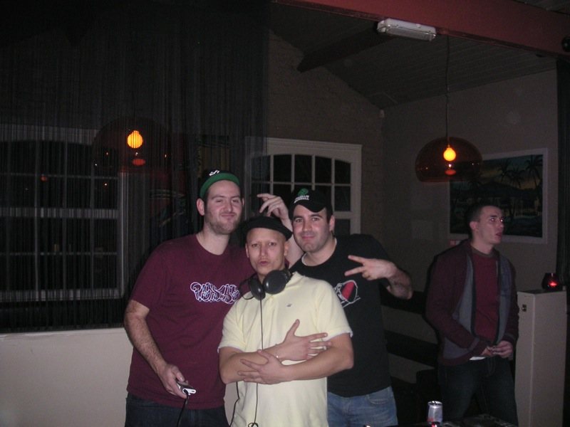 Four people posing together in a bar, one wearing headphones round his neck