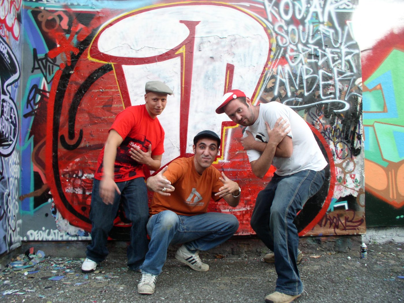 Three members striking poses in front of the IP wall