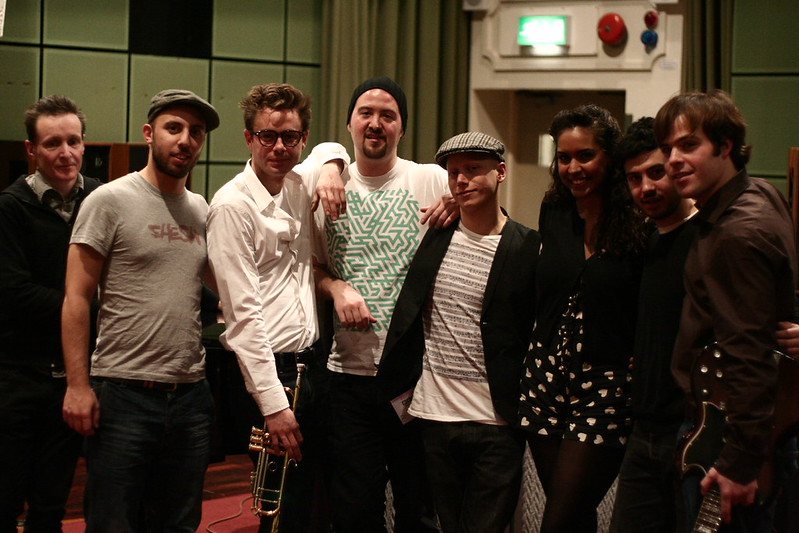 Eight people, including the band and singer, posing together in a studio